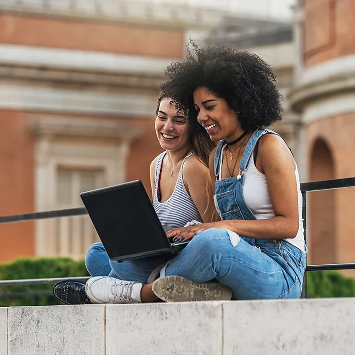 2 women students using a laptop outside.